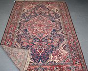 A North-west Persian rug, early/mid-20th Century, the dark blue field with a red palmette-filled medallion supported by further palmettes and flowerheads, within a red complimentary border, approx 217cm x 143cm.