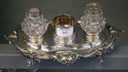 A Victorian silver inkstand, fitted with a central cylindrical box flanked by a pair of silver mounted cut glass bottles, the stand of shaped oval form with foliate scroll rim and scroll feet, London 1848 by Edward, John and William Barnard, length approx 26.5cm (central box lacking chamberstick cover).