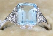 An aquamarine and diamond ring, mounted with the rectangular step cut aquamarine between diamond set three stone shoulders.