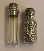 A late Victorian cylindrical clear glass scent bottle and stopper with scroll embossed silver collar and hinged lid, Birmingham 1890, together with a George V silver cased scent bottle and stopper with foliate scroll decoration, London 1934.