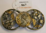 An Art Nouveau plated and parcel gilt nurse's buckle, designed as a pair of pierced and embossed floral roundels centred with a smaller circular panel depicting a head and shoulders portrait of a maiden framed by convolvulus, impressed 'P. Bryk'.