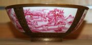 A Chinese porcelain circular bowl, mark of Qianlong but probably late 19th Century, the exterior painted with four pink landscape panels within gilt and black borders, four character mark of Qianlong in blue enamel to base (hairline crack), together with a Chinese Canton famille rose cup, mid-19th Century, decorated with figures (faults).