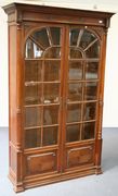 An early 20th Century walnut display cabinet, the dentil moulded cornice above two arched bevelled plate glass lattice doors flanked by turned and spiral fluted pilasters, on a plinth base, height approx 204cm, width approx 125cm.