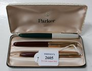 A Parker 51 magenta coloured plastic fountain pen with gilt metal cap and a matching ballpoint pen, within a Parker case, and a Parker green plastic fountain pen with gilt decorated white cap.