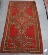 A Turkish rug, early 20th Century, the red field with three hooked medallions, within a complimentary border, approx 151cm x 80cm.