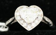 A diamond heart shaped cluster ring, claw set with a heart shaped diamond within a border of circular cut diamonds between diamond set four stone shoulders.