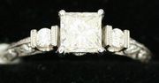 An 18ct white gold and diamond ring, claw set with the principle princess cut diamond between diamond set shoulders.
