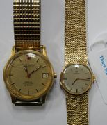 An Omega 9ct gold lady's bracelet wristwatch, the signed circular silvered dial with baton numerals, with thin black hands, on a tapering textured interwoven link bracelet, with a fold-over clasp, and an Omega Electronic Constellation gilt metal fronted wristwatch, the signed brushed gilt dial with baton numerals and a date-of-the-month aperture, on an expanding metal bracelet, with the original booklets.