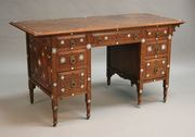 A late Victorian Arts and Crafts Middle Eastern style walnut twin pedestal desk, carved with overall geometric patterns and inlaid with bone and mother-of-pearl star motifs, the brown leather writing surface above an arrangement of seven drawers, raised on turned legs and castors, width approx 139cm (some faults).