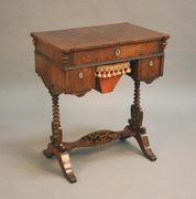 A mid-19th Century rosewood work table, the rectangular top sliding to reveal a compartmentalized interior fitted with silver sewing implements, the projected corners above drop finials and a Dutch ripple moulded frieze fitted with two drawers and a basket slide, raised on a pair of bobbin turned supports issuing scrolling brackets and downswept sabre legs united by a shaped stretcher, width approx 62cm.