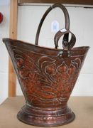 A late 19th/early 20th Century copper coal scuttle, the loop handle above an Art Nouveau floral design, together with a pair of tongs.