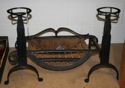 An early 20th Century wrought iron fire basket of curved form, with matching dogs with circular tops.