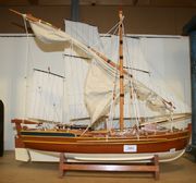 A late 20th Century model of a three-masted sailing boat with half-painted hull, the detailed deck mounted with eight cannons and dinghy, overall length approx 80cm, together with a single-masted sailing and rowing boat with half-painted hull, the detailed deck mounted with three cannons, overall length approx 60cm.