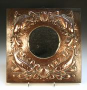 An Arts and Crafts Newlyn copper wall mirror, the tondo bevelled glass mirror within a relief surround of four fish and two scallop shells on a hammered background, stamped 'Newlyn', approx 49cm x 48.5cm.