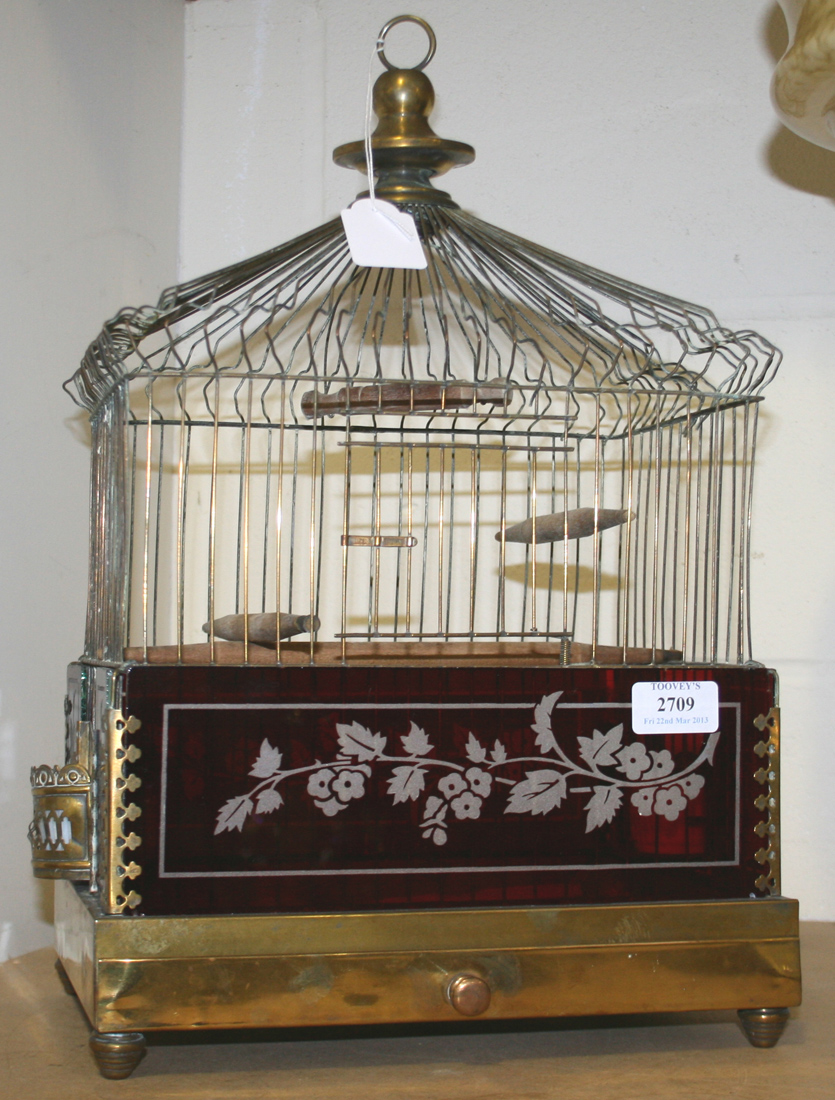 An Edwardian brass birdcage, the sides inset with acid etched ruby glass  panels, the feeding doors b