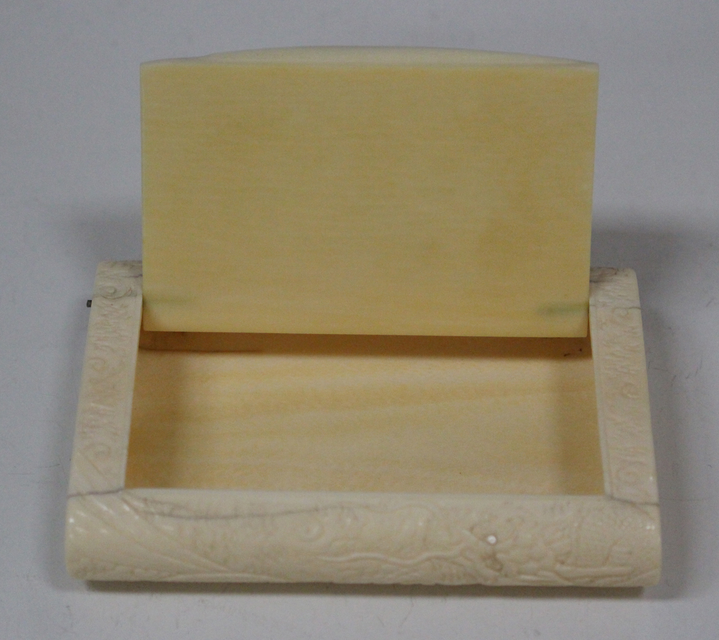 A Japanese ivory cigarette case, early 20th century, of curved rectangular  form, carved in low relie