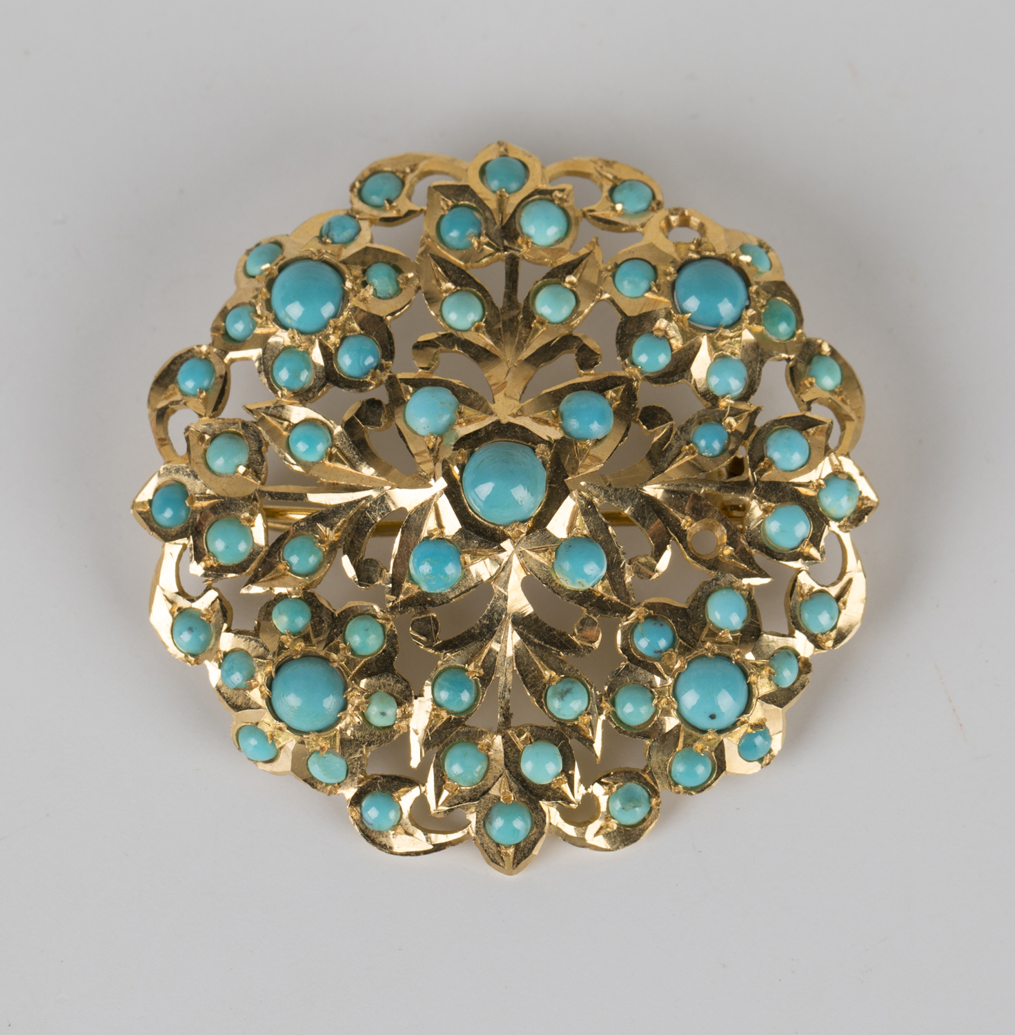 A gold and turquoise brooch of shaped circular form with floral and ...