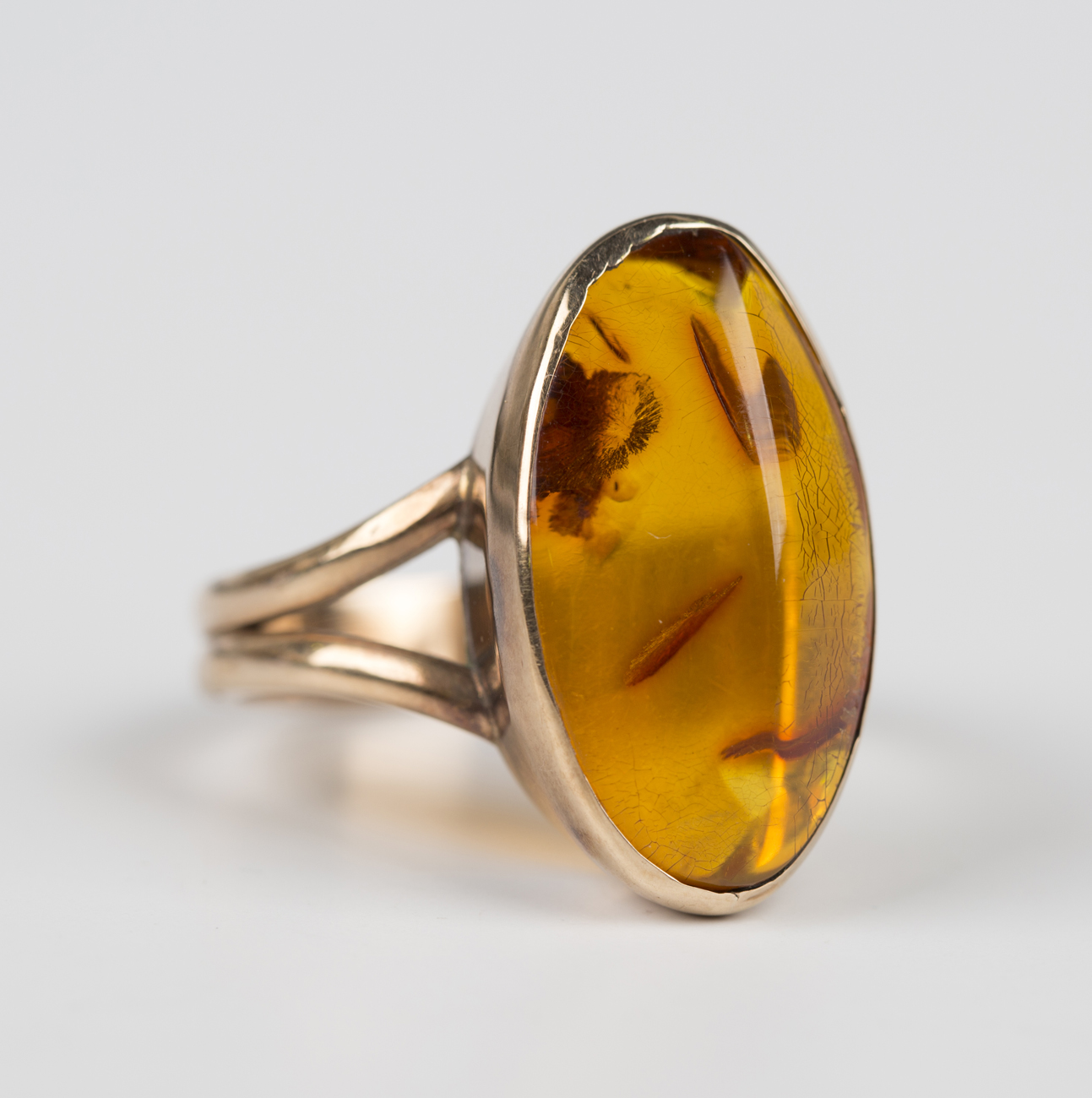 A gold ring, mounted with an oval amber between split shoulders ...
