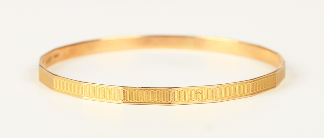 A 9ct gold faceted circular bangle with engine turned decoration ...