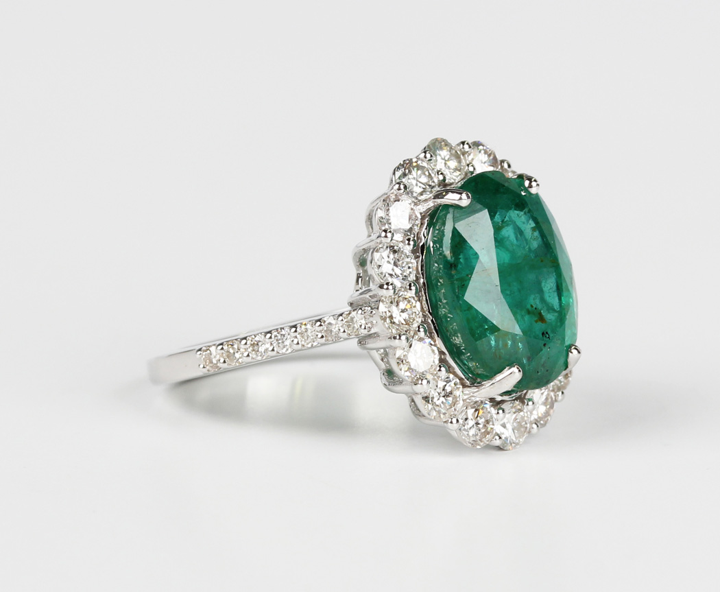 A white gold, emerald and diamond cluster ring, claw set with the large ...